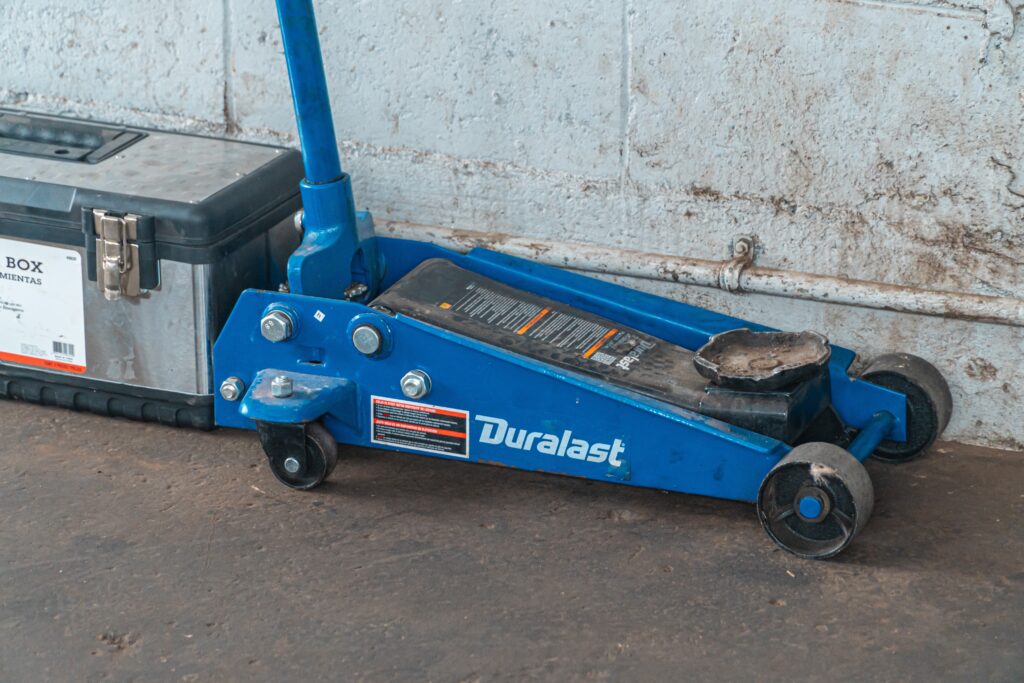 A blue floor jack in a garage, ready to lift a car.