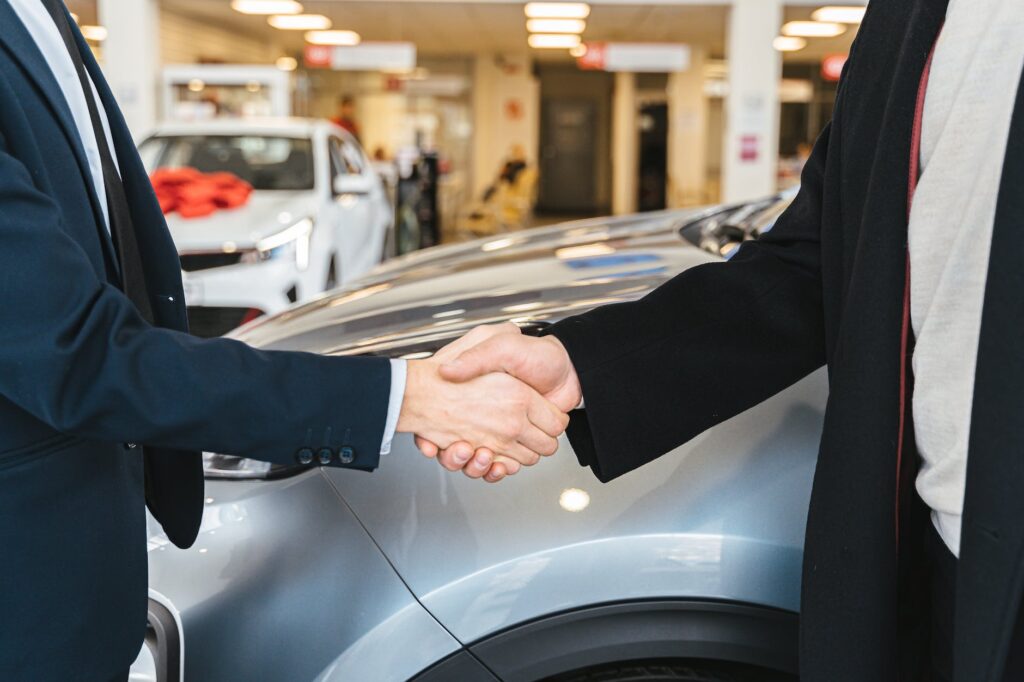 close up of men shaking hands and cars in background